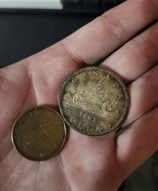 A 1963 Canadian silver dollar next to a modern Canadian loonie, both resting in a hand.